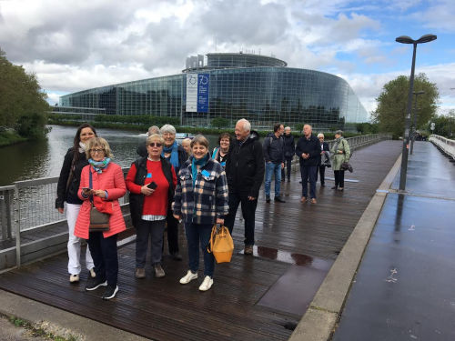 Die Gruppe steht vor dem Gebäude des Europarats auf einer Brücke auf regenasser Straße